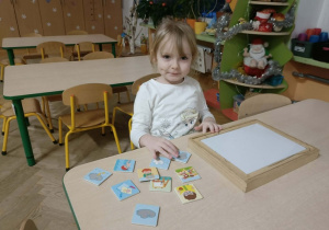 Dziewczynka w białej bluzce siedzi przy stoliku i układa układankę magnetyczną.