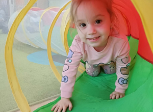 Dziewczynka w różowej bluzie przechodzi przez kolorowy tunel.