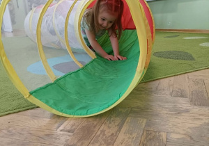 Dziewczynka w dwóch kucykach przechodzi przez kolorowy tunel.