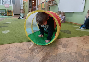 Chłopiec w czarno-szarej bluzce przechodzi przez kolorowy tunel.