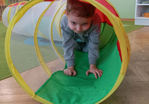 Chłopiec w szarej bluzie przechodzi przez kolorowy tunel.