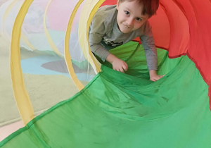 Chłopiec w zielonej bluzce przechodzi przez kolorowy tunel.