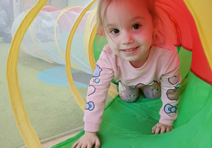 Dziewczynka w różowej bluzie przechodzi przez kolorowy tunel.