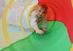 Dziewczynka w białej bluzie przechodzi przez kolorowy tunel.