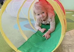 Dziewczynka w różowej bluzce z falbankami przechodzi przez kolorowy tunel.