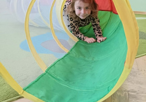 Dziewczynka w bluzce w panterkę przechodzi przez kolorowy tunel.