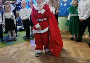 Chłopiec przebrany za Mikołaja recytuje wiersz. W tle stoją dzieci.