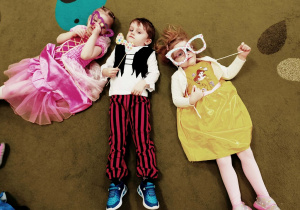 Dwie dziewczynki i chłopiec leżą na dywanie z rekwizytami do fotobudki.