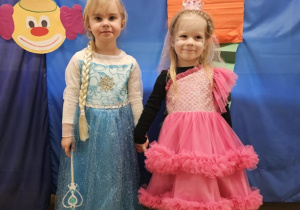 Dwie dziewczynki przebrane za księżniczki pozują na tle niebieskiej tablicy.