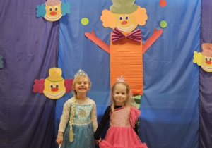 Dwie dziewczynki przebrane za księżniczki pozują na tle niebieskiej tablicy.