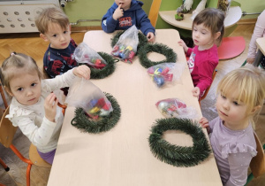 Grupa dzieci siedzi wokół stołu. Na stole leżą wianki i ozdoby w torebeczkach.