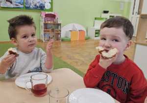 Dwóch chłopców siedzi przy stoliku i je pączki.