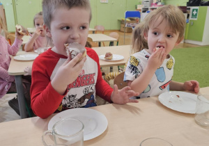 Dwóch chłopców siedzi przy stoliku i je pączki.