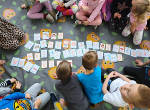 Na dywanie w sowy leżą karty. Wokół kart siedzą dzieci.