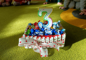 Na zielonym dywanie stoi tort ze słodyczy.