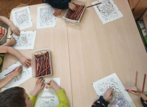 dzieci siedzą przy stoliku i kolorują kolorowanki z okazji Dnia Babci i Dziadka