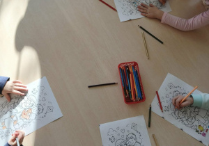 dzieci siedzą przy stoliku i kolorują kolorowanki z okazji Dnia Babci i Dziadka