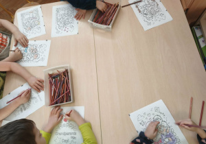 dzieci siedzą przy stoliku i kolorują kolorowanki z okazji Dnia Babci i Dziadka