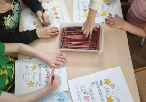 dzieci siedzą przy stoliku i kolorują kolorowanki z okazji Dnia Babci i Dziadka
