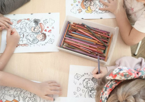 dzieci siedzą przy stoliku i kolorują kolorowanki z okazji Dnia Babci i Dziadka