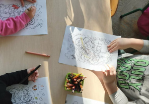 dzieci siedzą przy stoliku i kolorują kolorowanki z okazji Dnia Babci i Dziadka