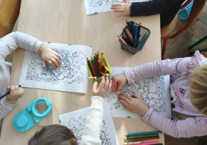 dzieci siedzą przy stoliku i kolorują kolorowanki z okazji Dnia Babci i Dziadka