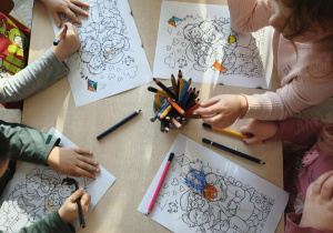 dzieci siedzą przy stoliku i kolorują kolorowanki z okazji Dnia Babci i Dziadka