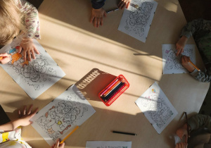 dzieci siedzą przy stoliku i kolorują kolorowanki z okazji Dnia Babci i Dziadka