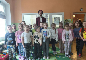 Grupa dzieci uśmiecha się do zdjęcia. Z tyłu stoi iluzjonista.