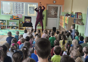 Iluzjonista stoi z młotkiem na nosie. Dzieci oglądają pokaz.