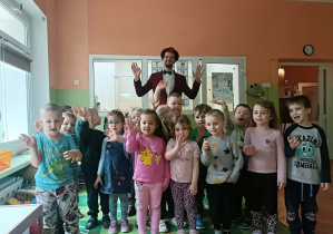 Grupa dzieci uśmiecha się do zdjęcia. Z tyłu stoi iluzjonista.