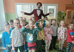 Grupa dzieci uśmiecha się do zdjęcia. Z tyłu stoi iluzjonista.