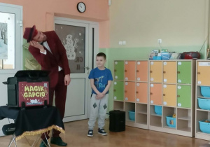 Na scenie stoi iluzjonista i chłopiec w niebieskiej bluzce.