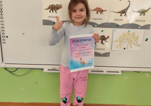 Dziewczynka uśmiecha sie trzymajac w rękachdyplom i nagrodę