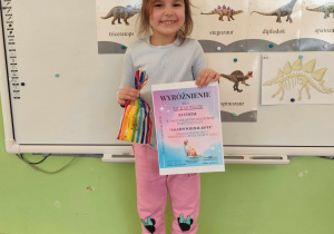 czynka uśmiecha sie trzymajac w rękachdyplom i nagrodę