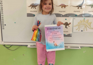 czynka uśmiecha sie trzymajac w rękachdyplom i nagrodę