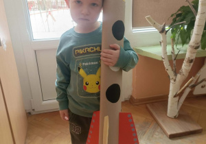 Chłopiec stoi z wykonaną rakietą na tle okna.