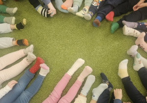 Na zielonym dywanie widać kolorowe skarpetki dzieci.