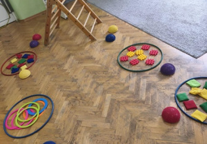 Na parkiecie stoją elementy do ścieżki sensorycznej ułożone w kolorowych kołach,