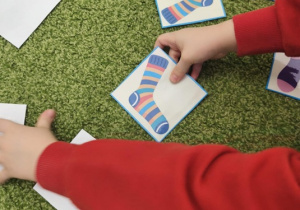 Dziecko w czerwonej bluzie otwiera karty z kolorowymi skarpetkami.