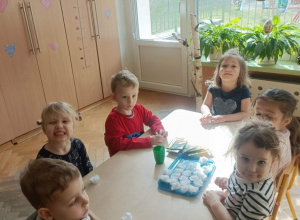 Szóstka dzieci siedzi wokół stolika. Na stoliku leżą pojemniczki z watą i rzeżucha w torebeczkach.