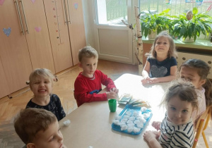 Szóstka dzieci siedzi wokół stolika. Na stoliku leżą pojemniczki z watą i rzeżucha w torebeczkach.