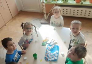 Szóstka dzieci siedzi wokół stolika. Na stoliku leżą pojemniczki z watą i rzeżucha w torebeczkach.