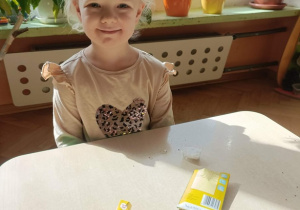 Dziewczynka siedzi przy stoliku. Na stoliku leżą pojemniczki z watą i rzeżucha w torebeczkach.