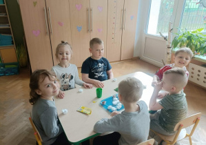 Szóstka dzieci siedzi wokół stolika. Na stoliku leżą pojemniczki z watą i rzeżucha w torebeczkach.
