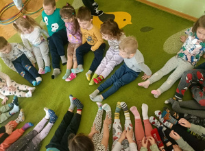 Na zielonym dywanie w kolorowych skarpetkach siedzą dzieci.