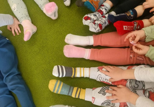 Na zielonym dywanie w kolorowych skarpetkach siedzą dzieci.