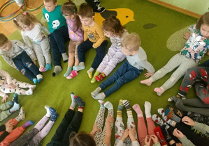Na zielonym dywanie w kolorowych skarpetkach siedzą dzieci.