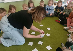 Pani w czarnej koszulce rozkłada karty. Dzieci siedzą wokół.