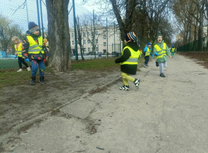 Dzieci w zielonych kamizelkach idą drogą.